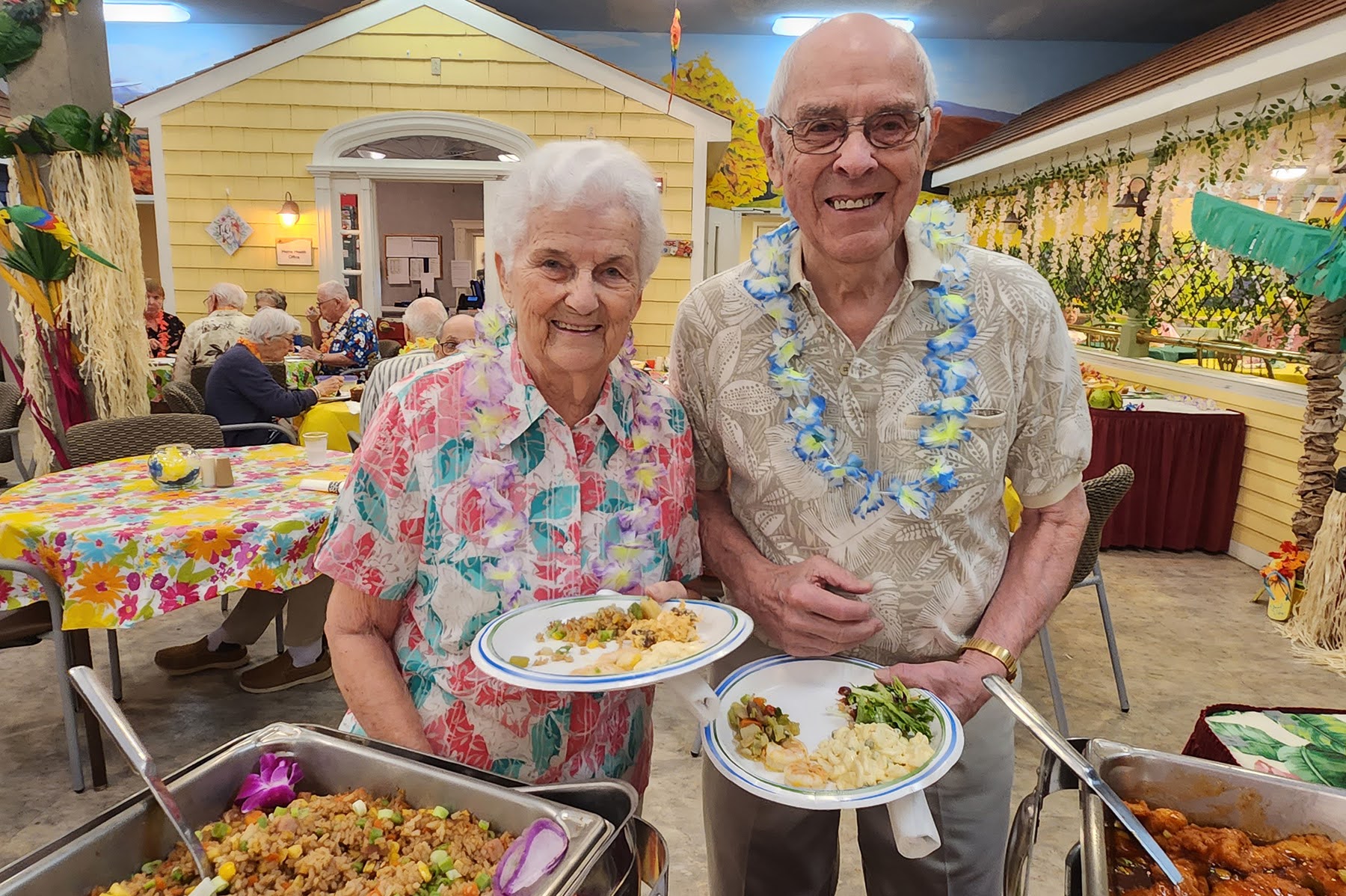 A woman and man holding plates of food at a Luau-themed buffet
