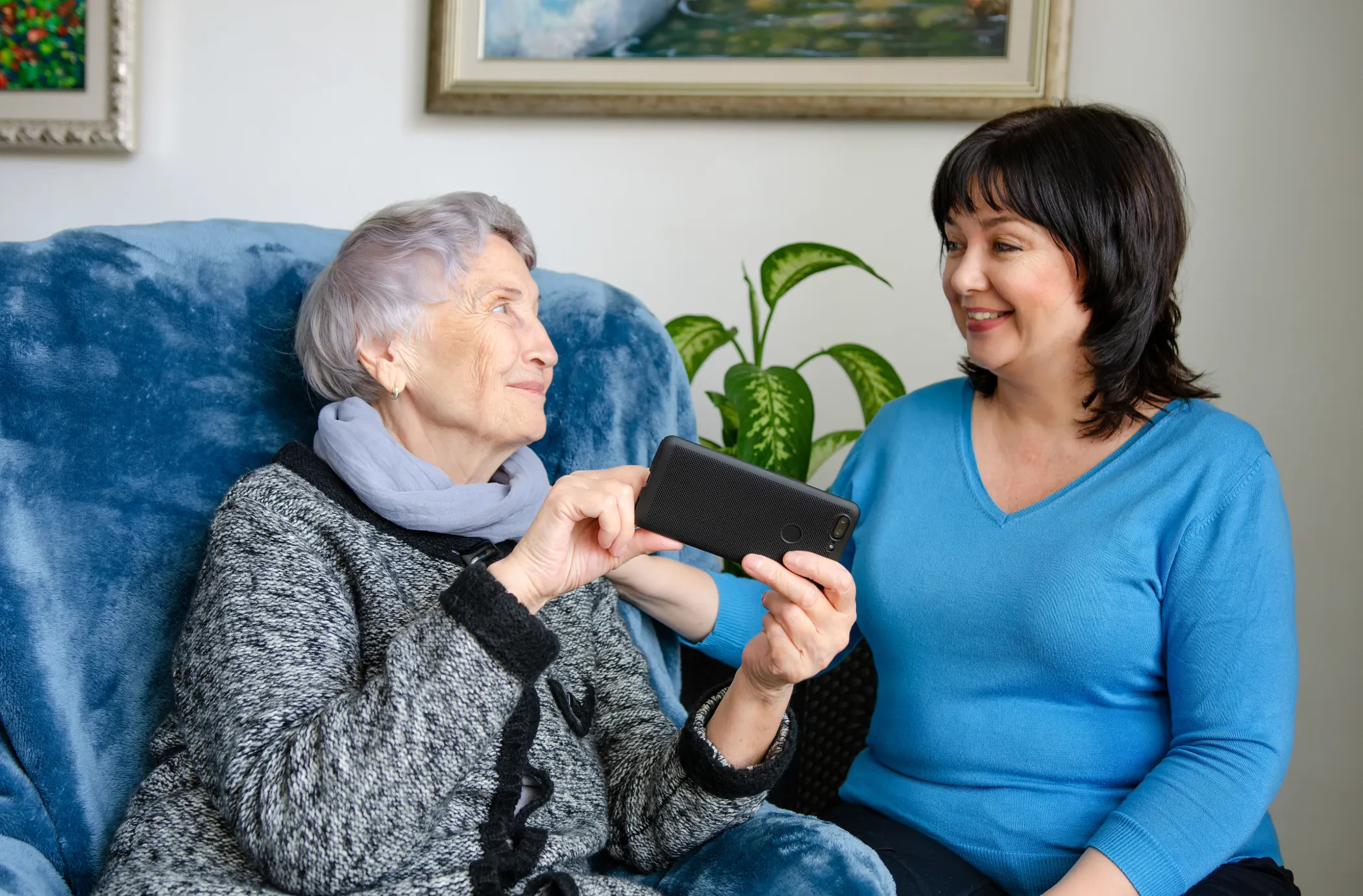 An older woman shares an image on her phone with a younger woman.